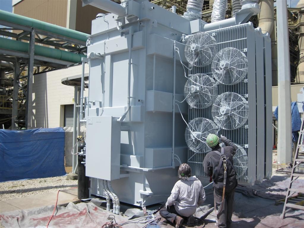 two men painting electrical transformer in substation