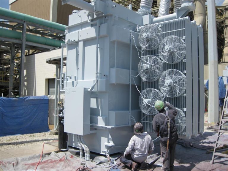 two men painting electrical transformer in substation